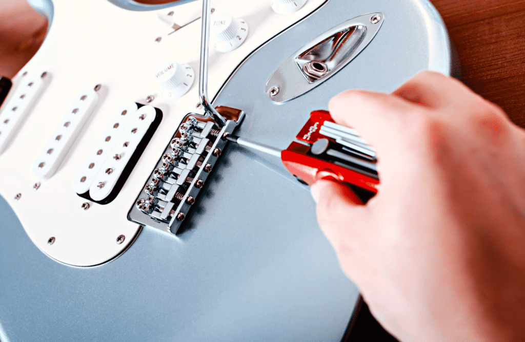 A guitar tech adjusting the saddles on a light blue fender stratocaster using an Ibanez MTZ11