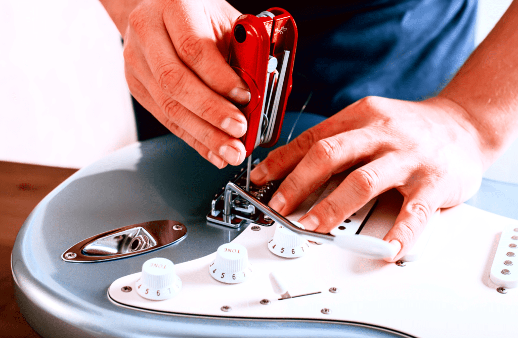 A guitar tech adjusting the action on a light blue fender stratocaster using an Ibanez MTZ11