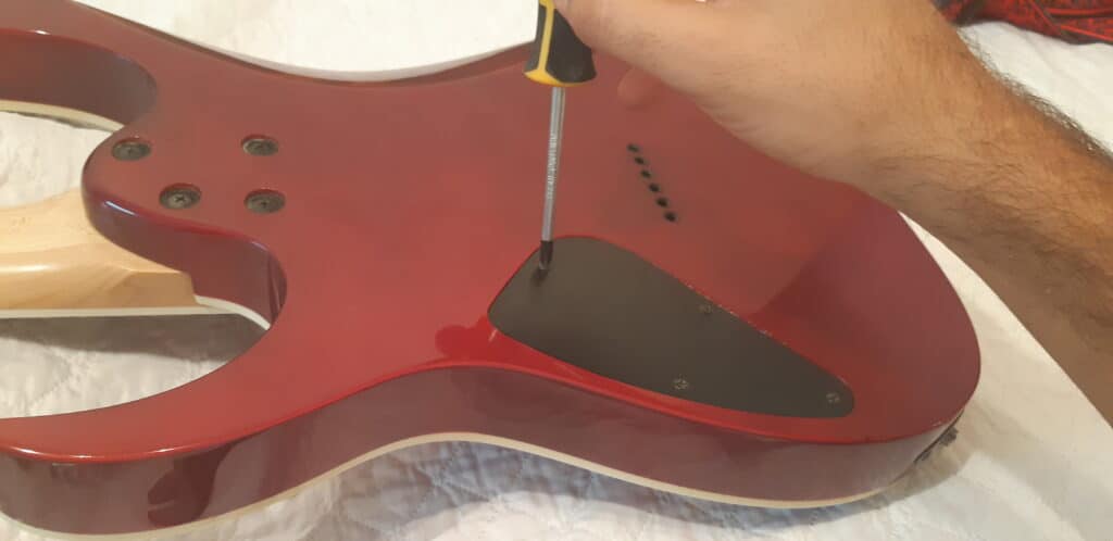 Opening the back cover of the guitar to access its electronics