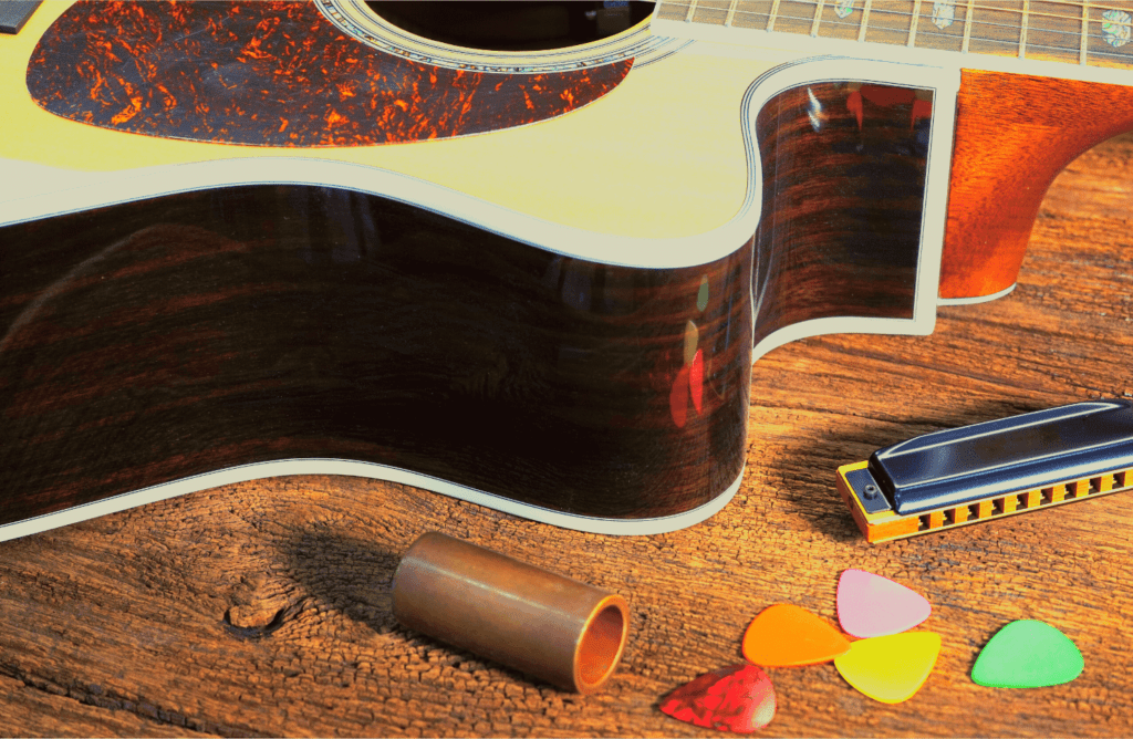 An acoustic guitar, a harmonica, guitar picks and a guitar slide